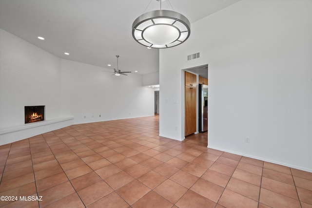 unfurnished living room with ceiling fan, a towering ceiling, and light tile patterned floors