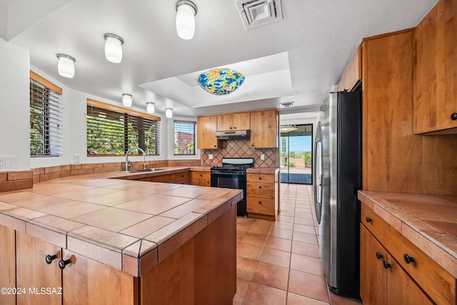 kitchen featuring tile countertops, stainless steel fridge, black range with electric stovetop, and sink