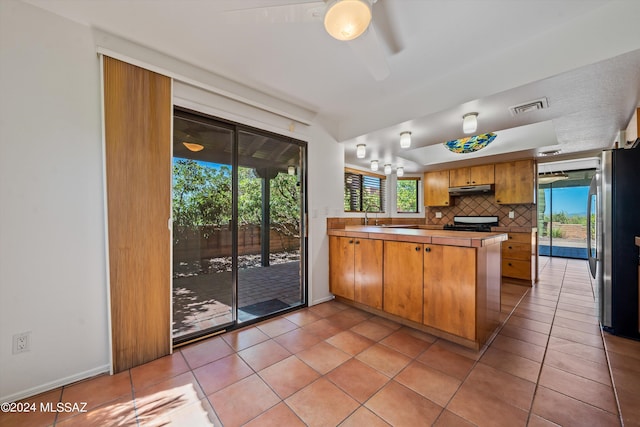 kitchen featuring sink, decorative backsplash, light tile patterned floors, kitchen peninsula, and stainless steel refrigerator