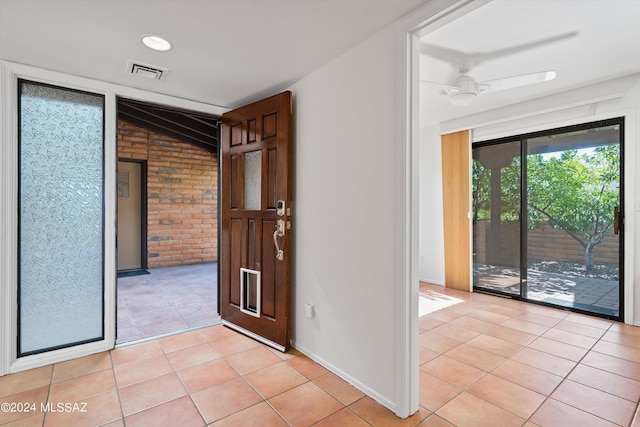 interior space featuring ceiling fan, light tile patterned floors, and brick wall