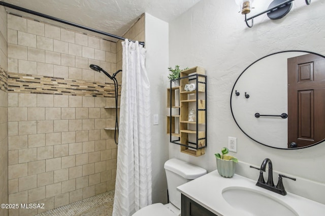 full bath featuring a textured wall, a tile shower, vanity, and toilet