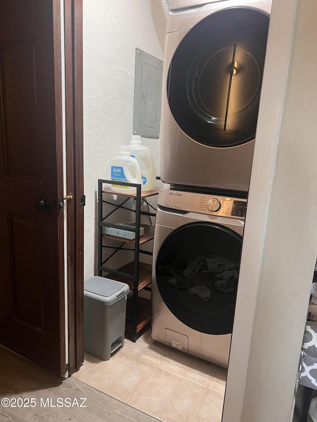 laundry area featuring light tile patterned floors, a textured wall, stacked washer and dryer, laundry area, and electric panel