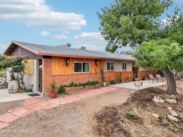 ranch-style home with brick siding, a patio, and roof with shingles