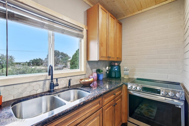 kitchen with dark stone counters, stainless steel electric range oven, brown cabinets, a sink, and backsplash