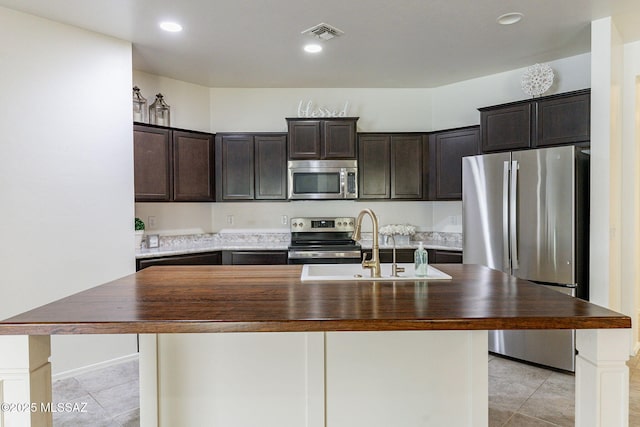 kitchen with wood counters, an island with sink, and appliances with stainless steel finishes