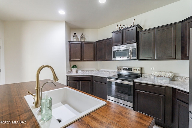 kitchen with light stone counters, sink, stainless steel appliances, and dark brown cabinets