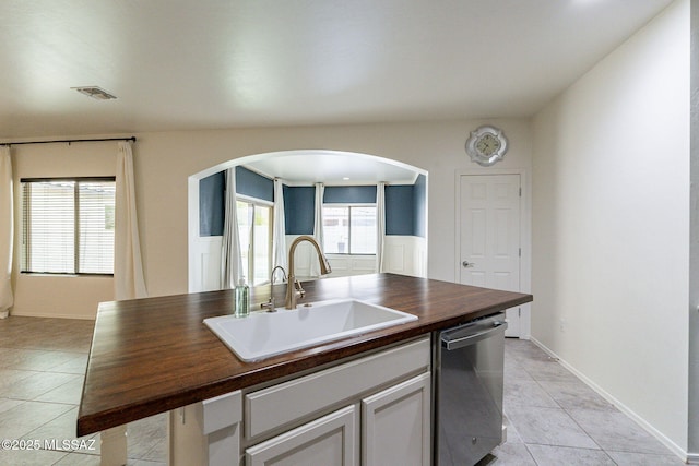 kitchen with a wealth of natural light, dishwasher, sink, wooden counters, and an island with sink