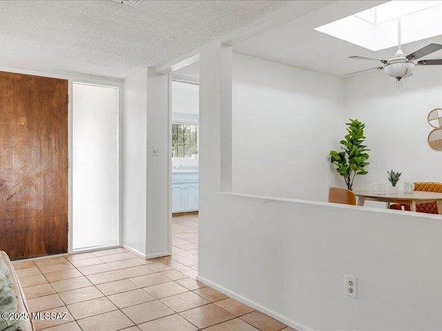 tiled entryway featuring a textured ceiling, ceiling fan, and a skylight