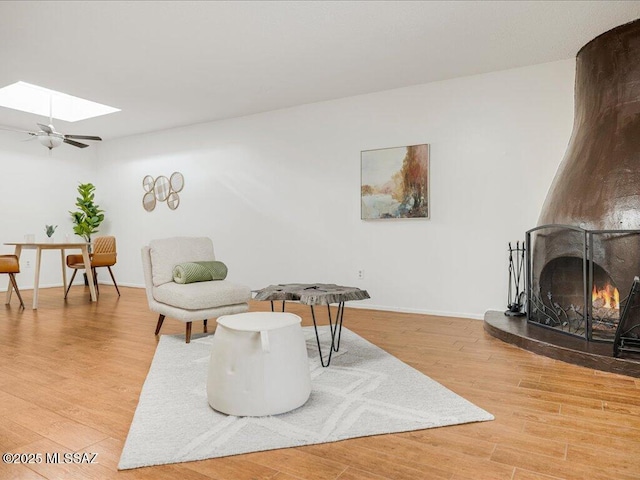 sitting room featuring ceiling fan, a skylight, hardwood / wood-style floors, and a fireplace