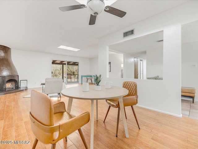 dining space featuring a fireplace, light wood-type flooring, and ceiling fan