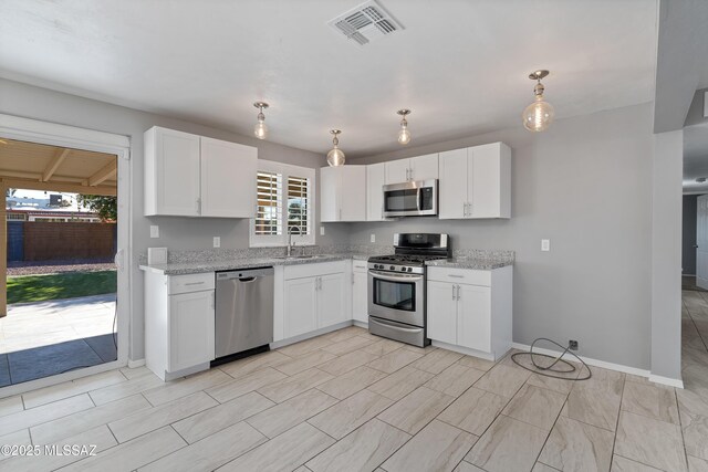 kitchen featuring appliances with stainless steel finishes, light stone counters, sink, white cabinets, and hanging light fixtures