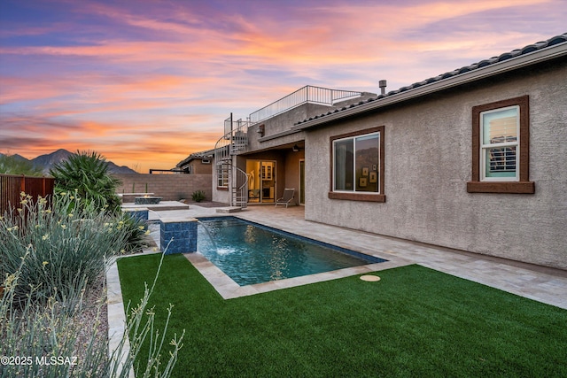 pool at dusk with a patio area, pool water feature, and a yard