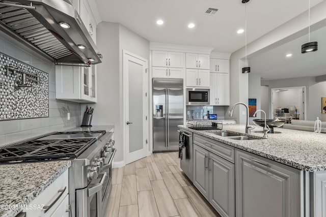 kitchen featuring light stone counters, sink, built in appliances, white cabinets, and range hood