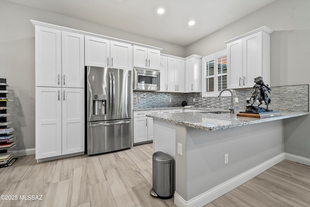 kitchen with kitchen peninsula, appliances with stainless steel finishes, light stone counters, sink, and white cabinetry