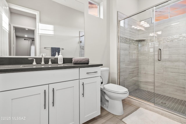 bathroom featuring a shower with door, vanity, and toilet