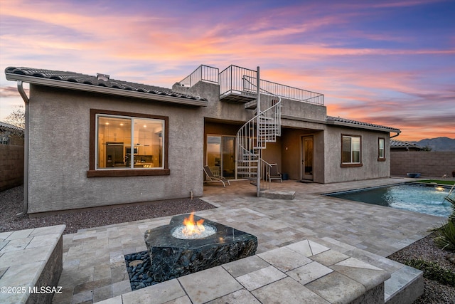 back house at dusk featuring a balcony, a fenced in pool, an outdoor fire pit, and a patio