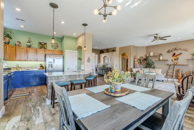 dining area featuring ceiling fan with notable chandelier, sink, and light wood-type flooring