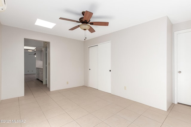 unfurnished bedroom featuring ceiling fan, a skylight, a closet, and light tile patterned floors