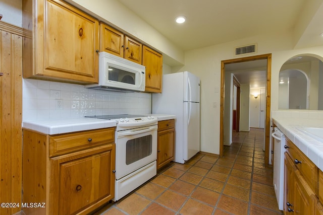 kitchen with backsplash, tile counters, dark tile patterned floors, and white appliances