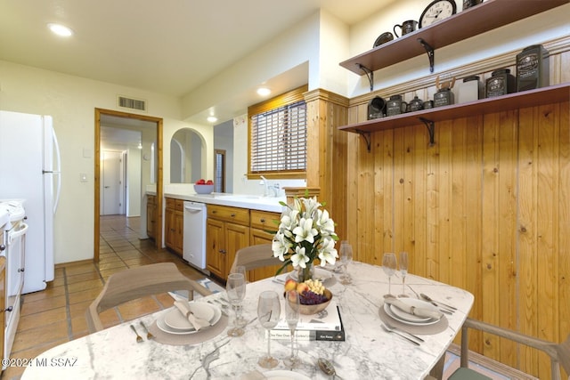 dining area with light tile patterned flooring, wooden walls, and sink