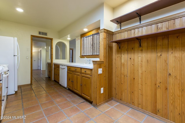 kitchen featuring light tile patterned flooring, white appliances, sink, and wooden walls