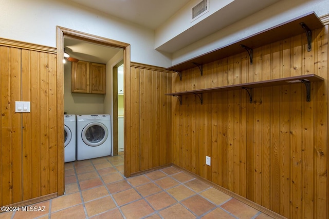 washroom featuring cabinets, wood walls, washing machine and dryer, and light tile patterned floors