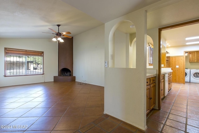 unfurnished living room with ceiling fan, washer and clothes dryer, lofted ceiling, a fireplace, and dark tile patterned flooring