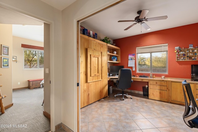 office area with ceiling fan, built in desk, and light carpet