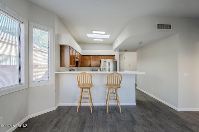 kitchen with stainless steel fridge with ice dispenser, a skylight, kitchen peninsula, and dark wood-type flooring