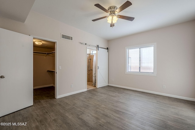 unfurnished bedroom featuring ceiling fan, dark hardwood / wood-style flooring, a barn door, a spacious closet, and a closet