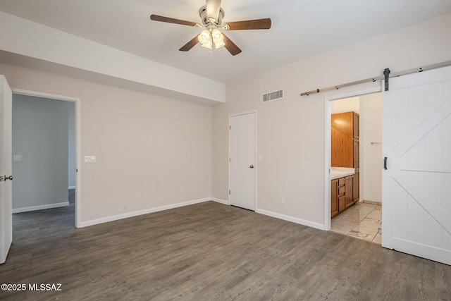 unfurnished bedroom with ensuite bath, a closet, ceiling fan, light hardwood / wood-style flooring, and a barn door