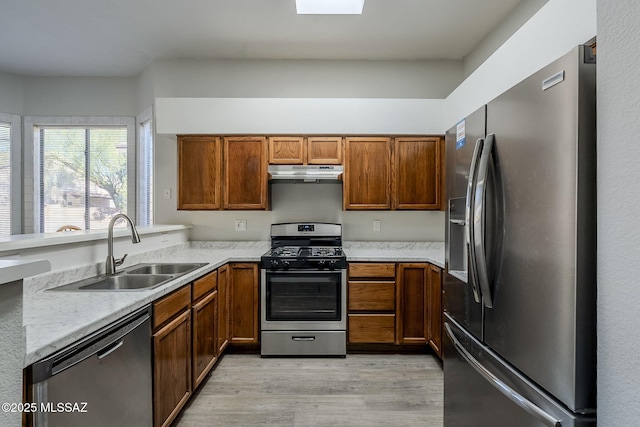 kitchen with sink, stainless steel appliances, light stone countertops, and light wood-type flooring