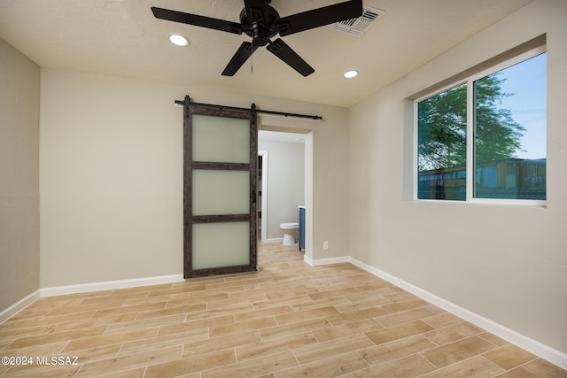 empty room featuring a barn door and ceiling fan