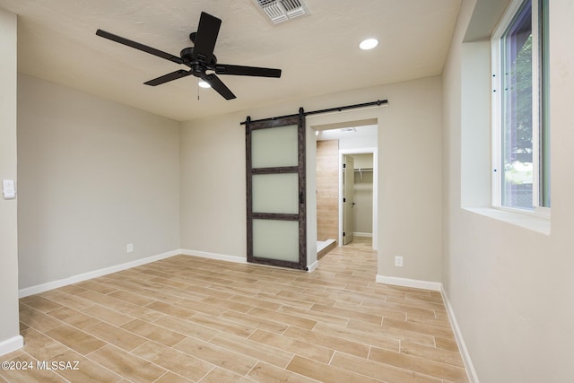 unfurnished room with ceiling fan, a barn door, and light hardwood / wood-style floors