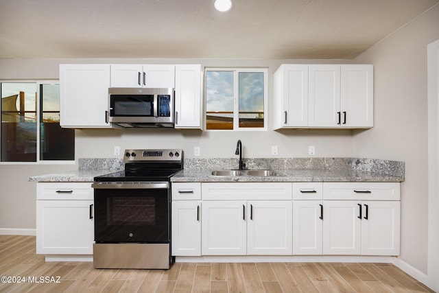 kitchen with light stone counters, sink, white cabinets, and stainless steel appliances