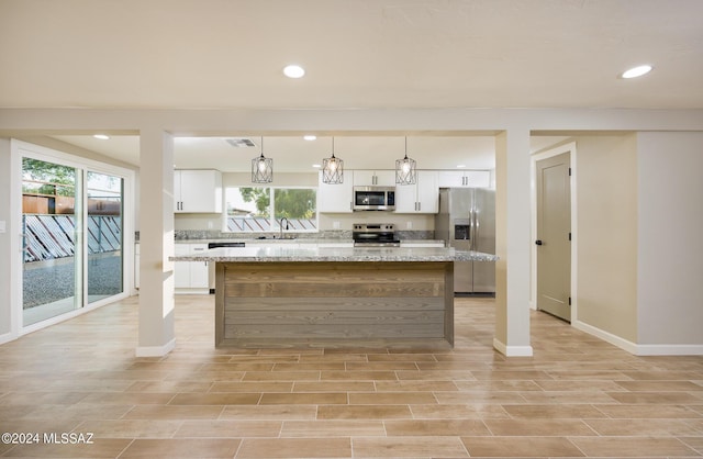 kitchen with hanging light fixtures, a kitchen island, light stone counters, white cabinets, and appliances with stainless steel finishes