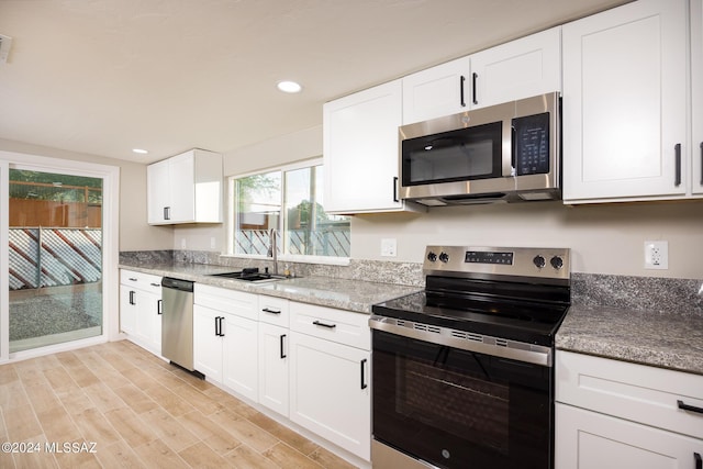 kitchen with stone counters, sink, stainless steel appliances, white cabinets, and light wood-type flooring