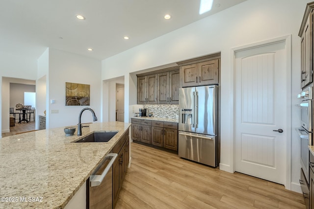 kitchen featuring light hardwood / wood-style floors, appliances with stainless steel finishes, tasteful backsplash, light stone counters, and sink