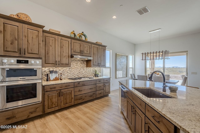 kitchen with appliances with stainless steel finishes, decorative light fixtures, a chandelier, light stone counters, and sink