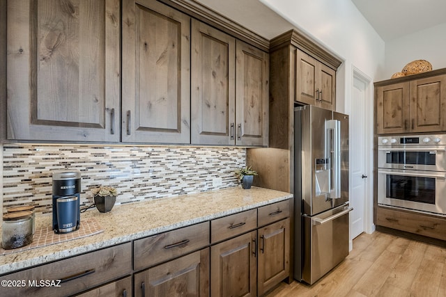 kitchen featuring decorative backsplash, light stone countertops, stainless steel appliances, and light hardwood / wood-style floors