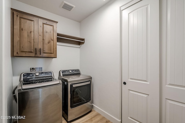 laundry room featuring light hardwood / wood-style flooring, washing machine and clothes dryer, and cabinets