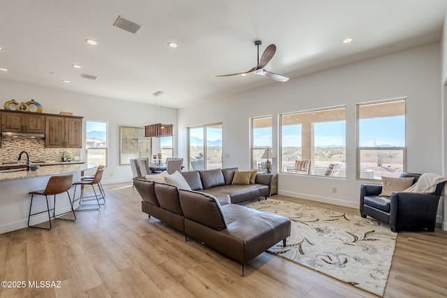 living room featuring ceiling fan, sink, and light wood-type flooring