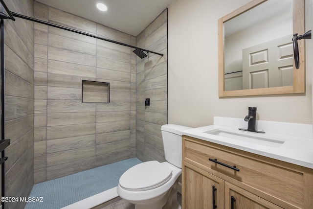 bathroom featuring a tile shower, vanity, and toilet