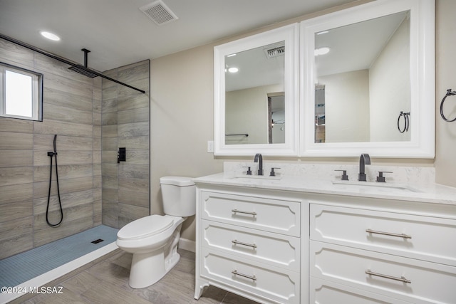 bathroom with hardwood / wood-style floors, vanity, toilet, and a tile shower