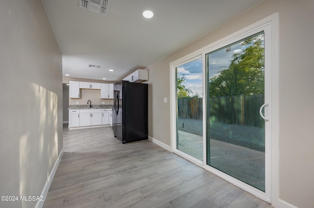 kitchen featuring black refrigerator, light stone counters, sink, light hardwood / wood-style floors, and white cabinetry