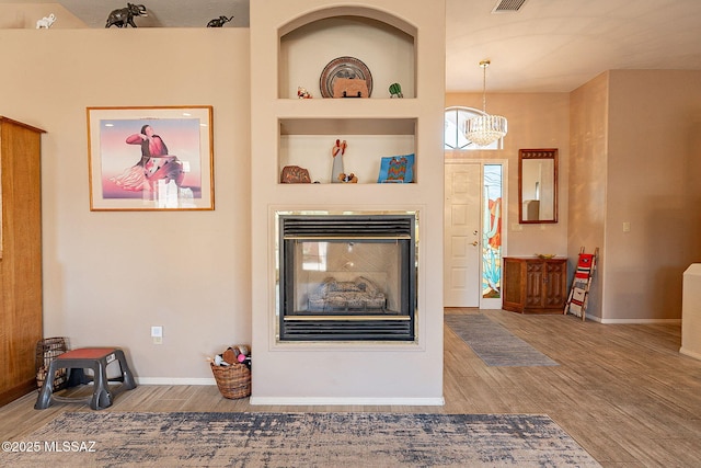 living room with hardwood / wood-style floors, built in shelves, and an inviting chandelier