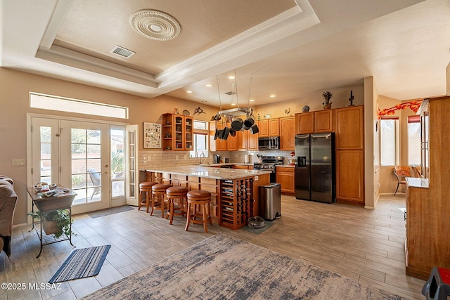 kitchen with backsplash, a kitchen breakfast bar, a raised ceiling, appliances with stainless steel finishes, and kitchen peninsula