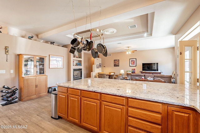 kitchen featuring beam ceiling, light stone counters, and ceiling fan