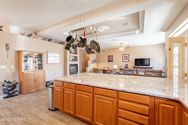 kitchen featuring ceiling fan, beam ceiling, and light stone countertops