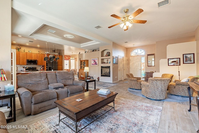 living room with light hardwood / wood-style floors, a raised ceiling, ceiling fan, and a healthy amount of sunlight